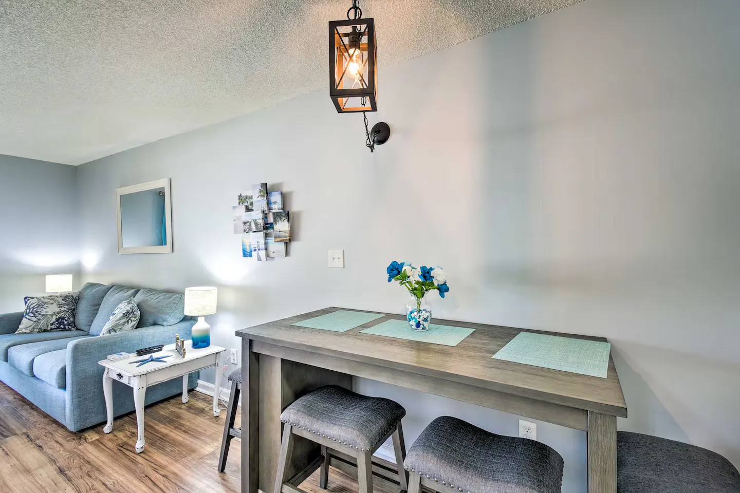 Dining counter with upholstered backless stools positioned next to a living room with a blue sofa.