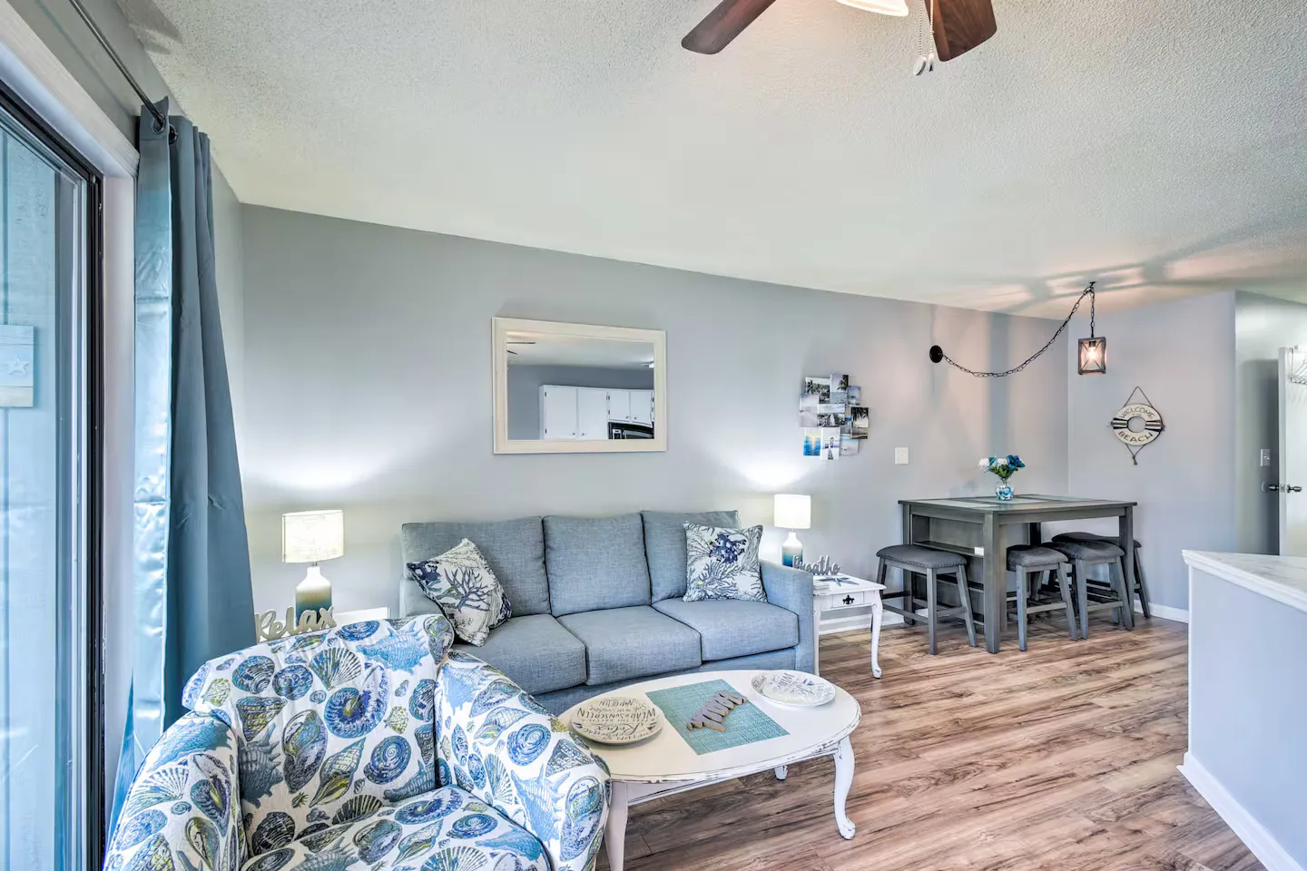 Living room featuring a blue sofa, seashell-patterned armchair, coffee table, and an adjacent high-top dining table with stools.