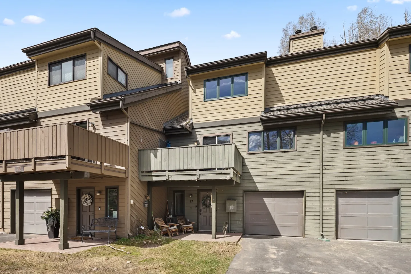 Exterior of multi-story townhomes with wood-paneled siding, attached garages, balconies, and entry doors under a clear sky.