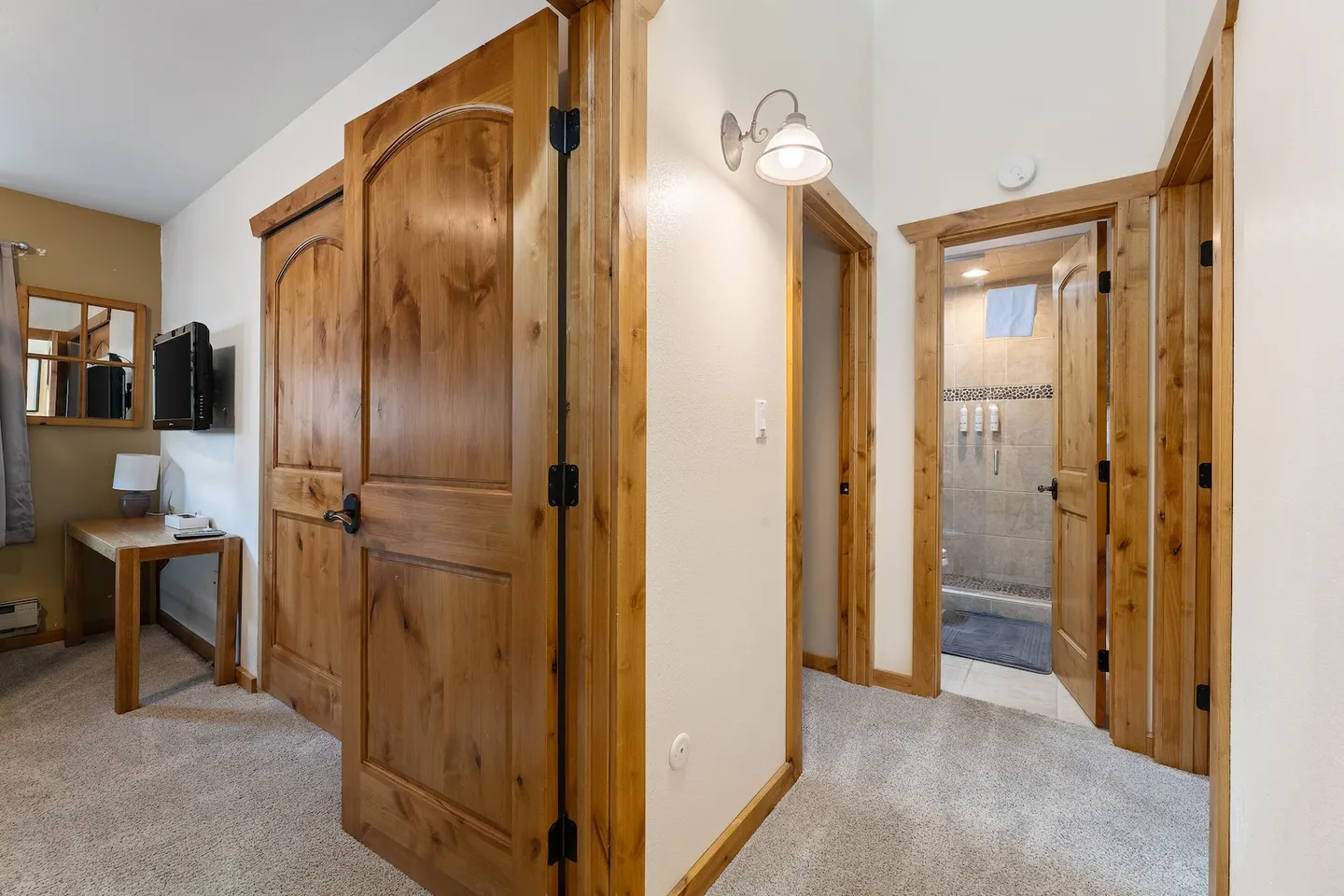 Hallway and bedroom entrance with solid wood doors, carpeted flooring, and a view into a tiled bathroom.