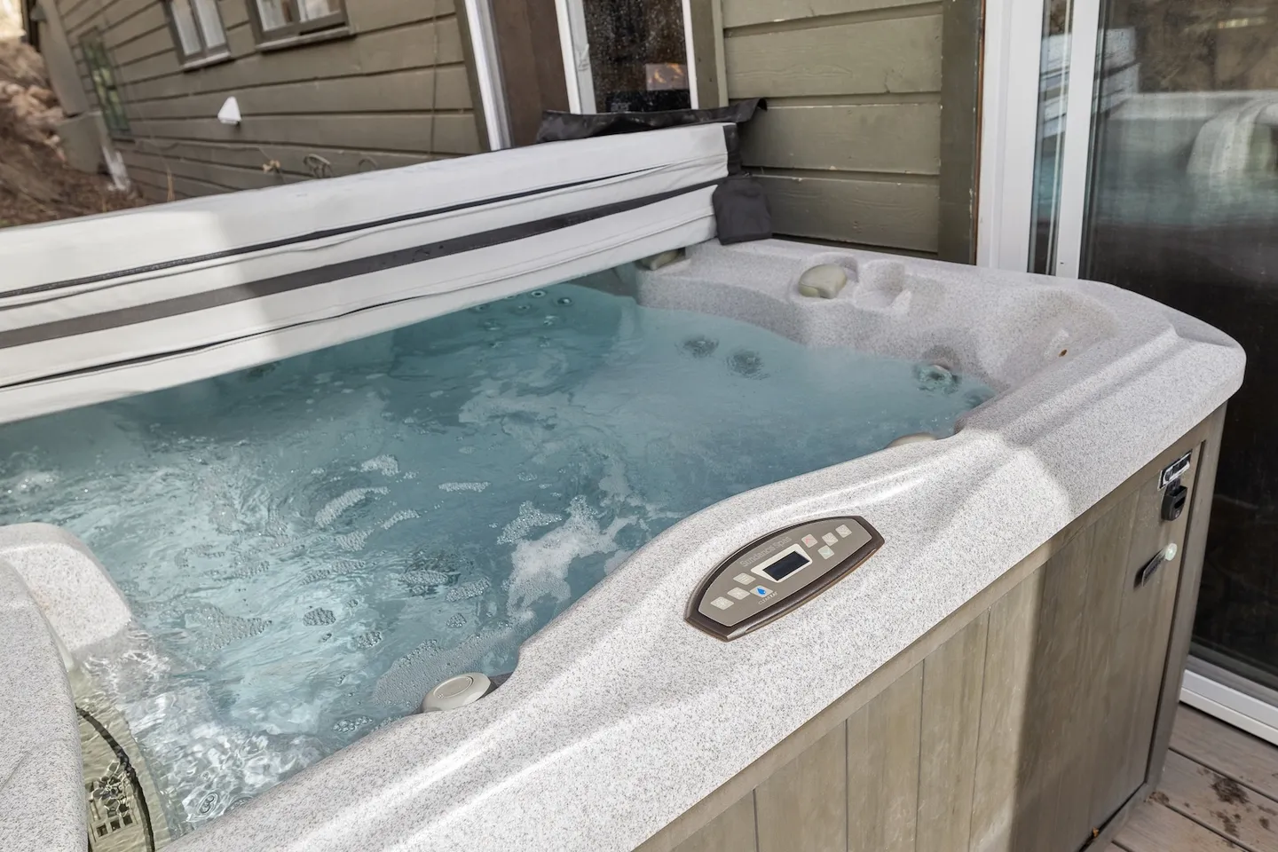 Close-up view of an outdoor hot tub with bubbling water next to a home's exterior wall.