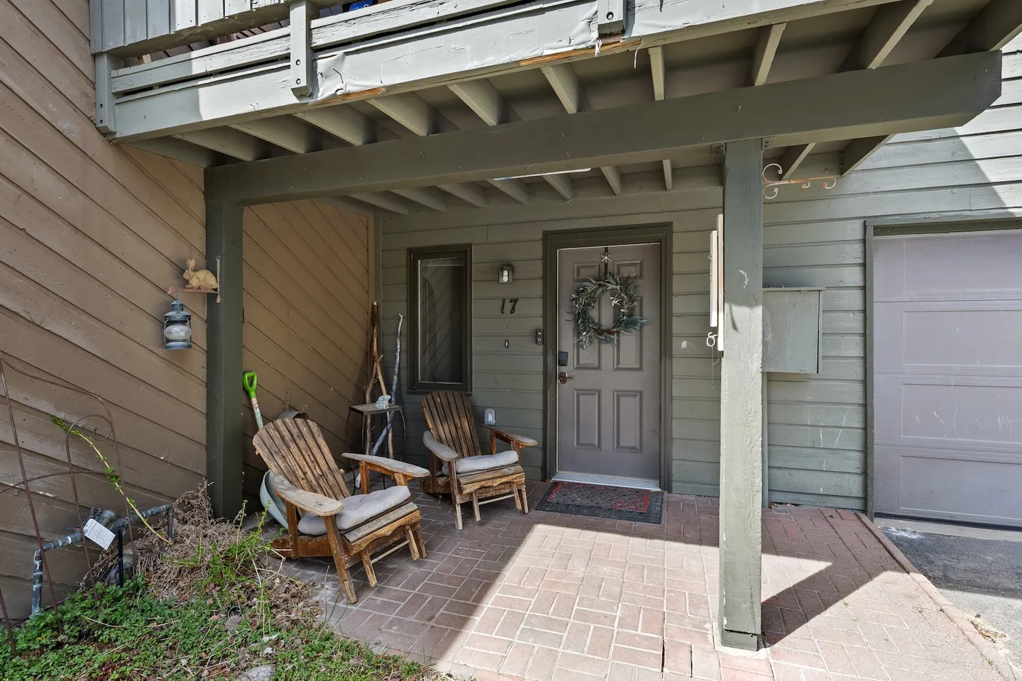 Covered brick entry patio with two rustic wooden armchairs next to a front door with a wreath.