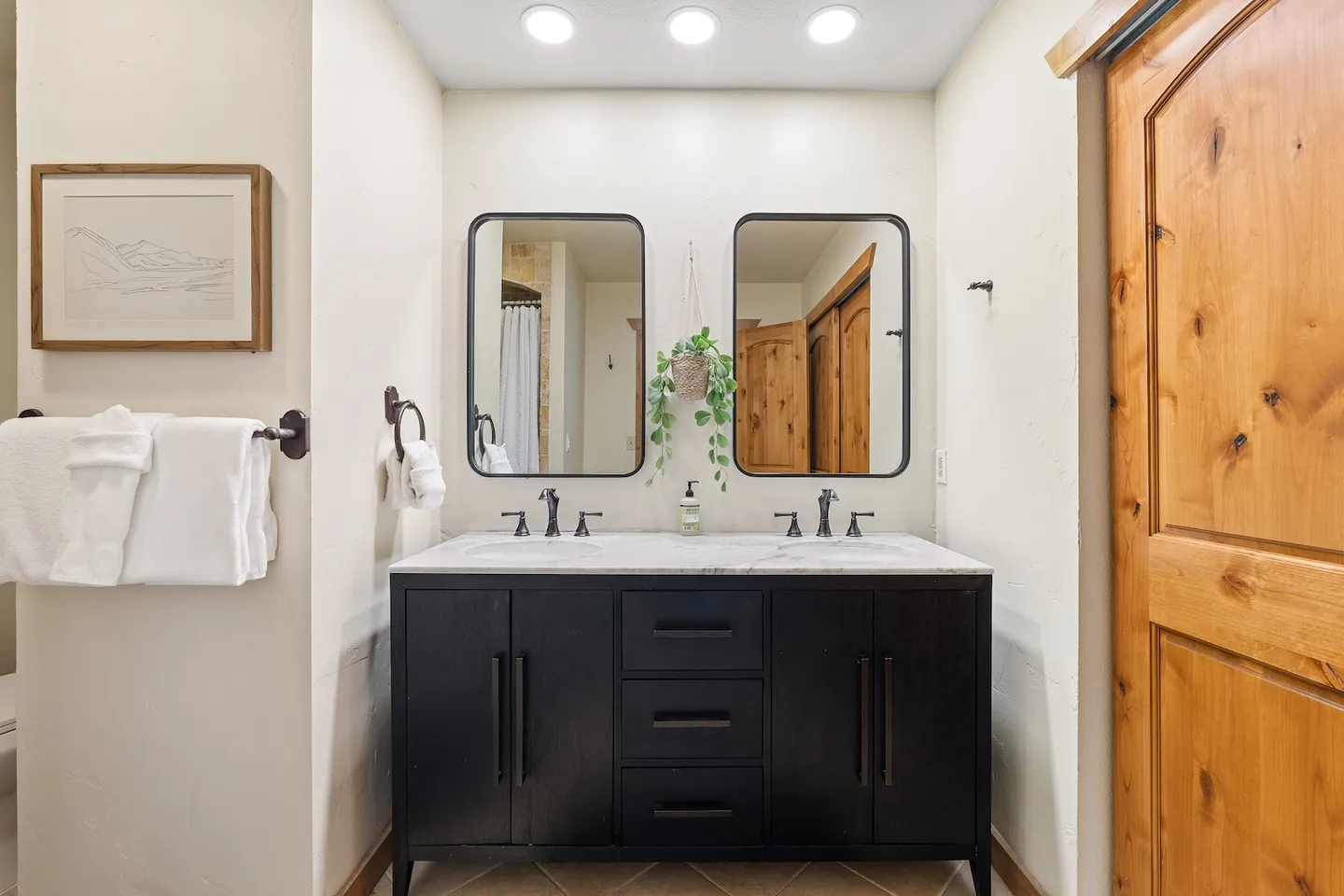 Bathroom vanity with a dark wood cabinet, double sinks, and two rounded-corner black-framed mirrors.