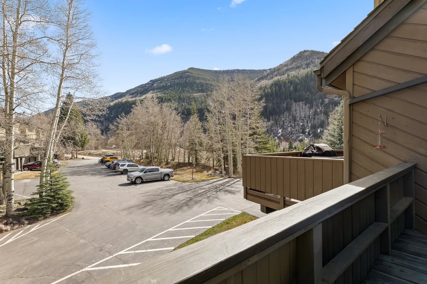 Balcony view overlooking a paved parking lot, trees, and forested mountains under a clear sky.