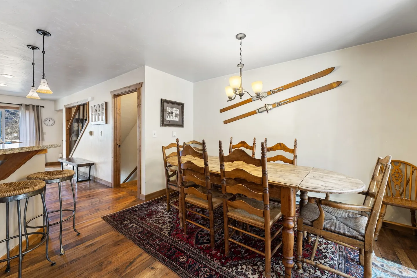 Dining area with a wooden oval table, matching chairs, ski decor on the wall, and wood floors over an area rug.