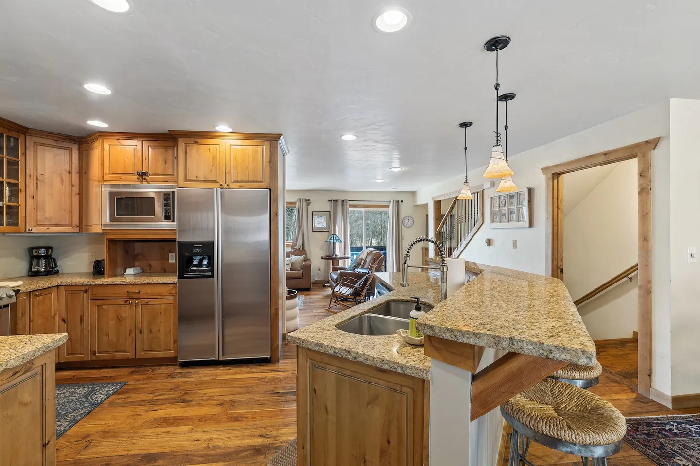Open-concept kitchen with wood cabinets, stone countertops, stainless steel appliances, and a raised breakfast bar looking toward the living area.