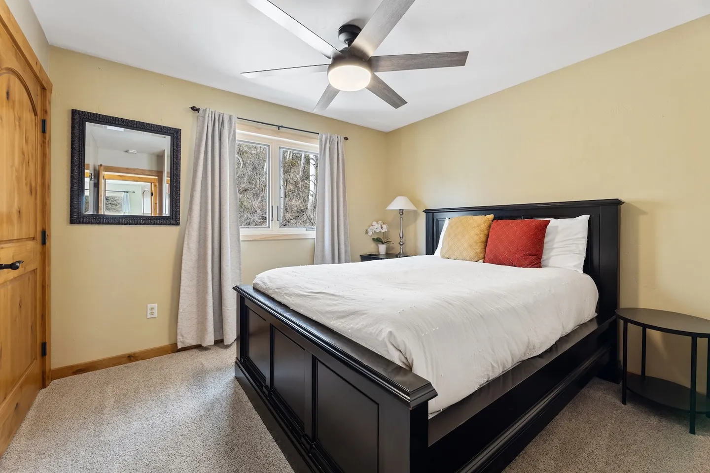 Bedroom with a dark wood bed frame, white bedding, ceiling fan, and carpeted floor.