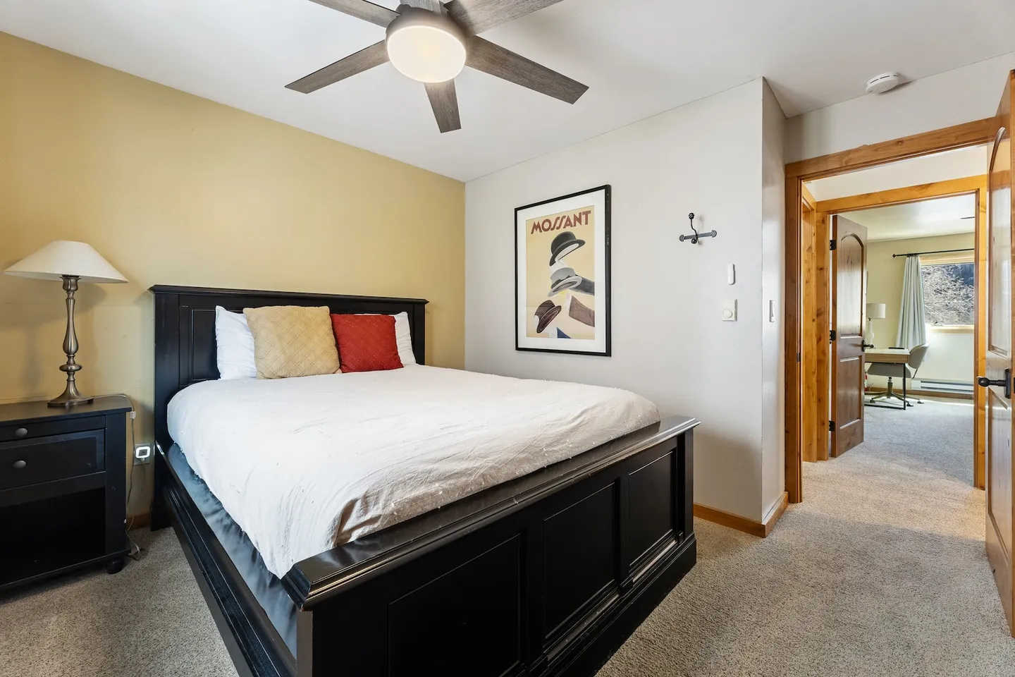 Bedroom with a dark wood bed frame, white bedding, ceiling fan, and open doorway leading to another room.
