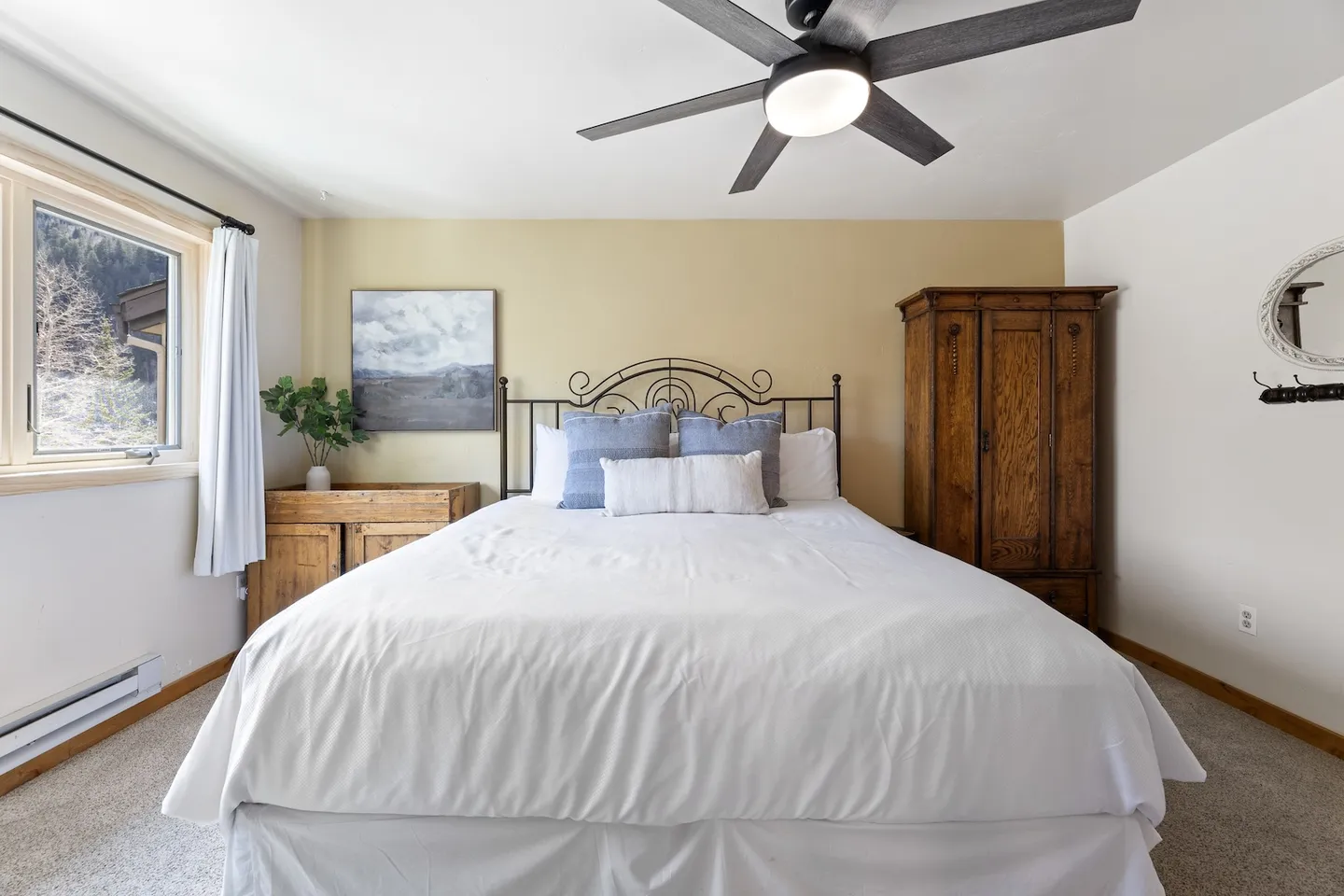 Bedroom with a metal-framed bed, white bedding, ceiling fan, wooden armoire, and a window with mountain views.