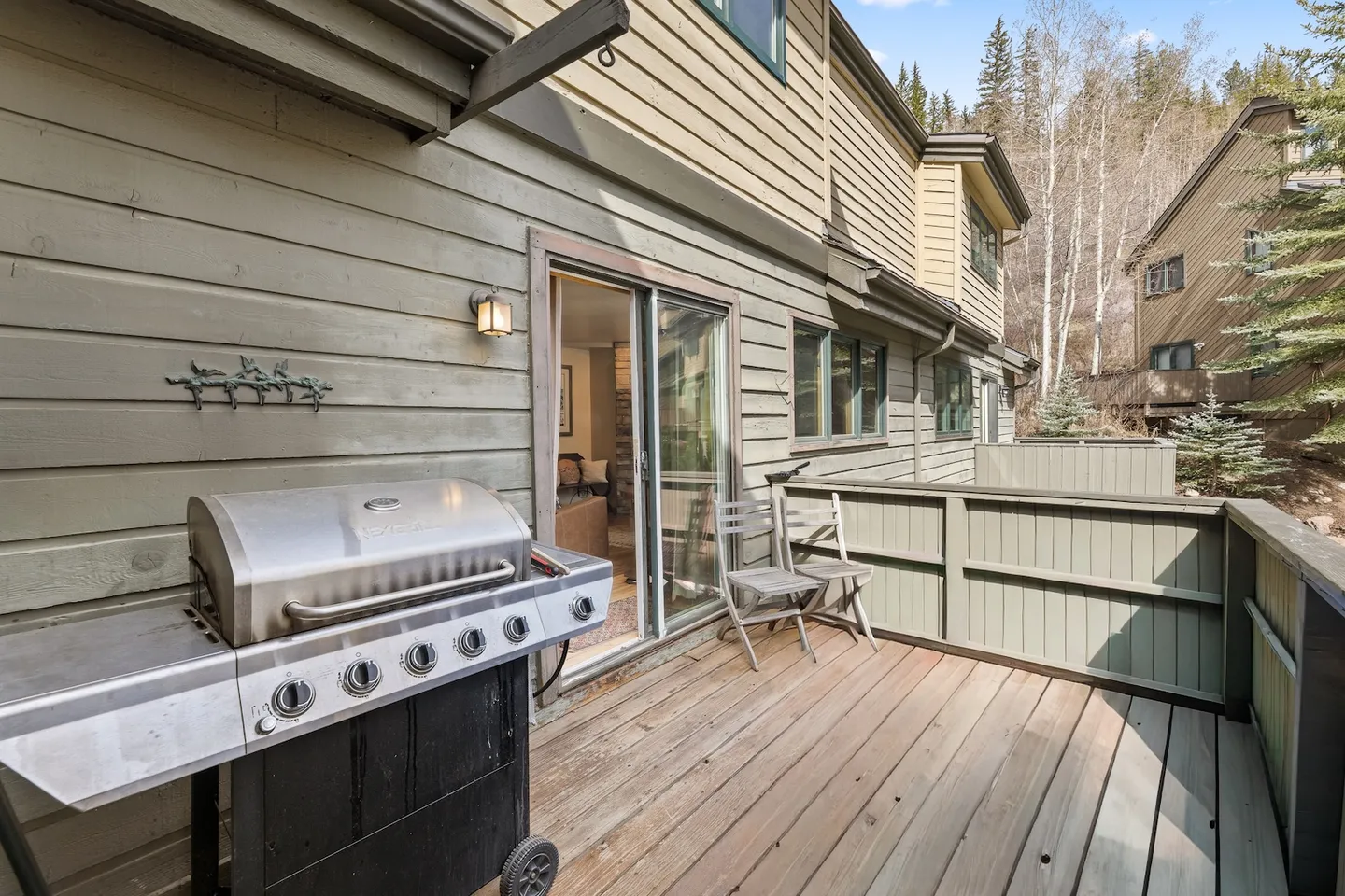 Outdoor wooden deck featuring a stainless steel barbecue grill, two folding chairs, and sliding glass door access to the interior.