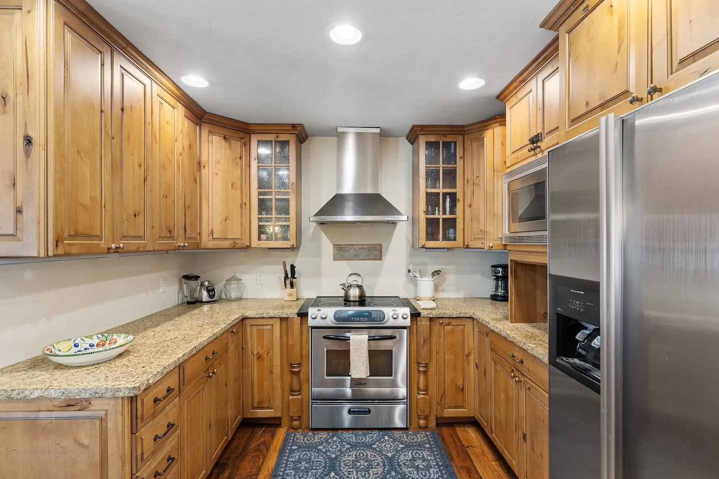 U-shaped kitchen with natural wood cabinets, granite countertops, and stainless steel appliances.