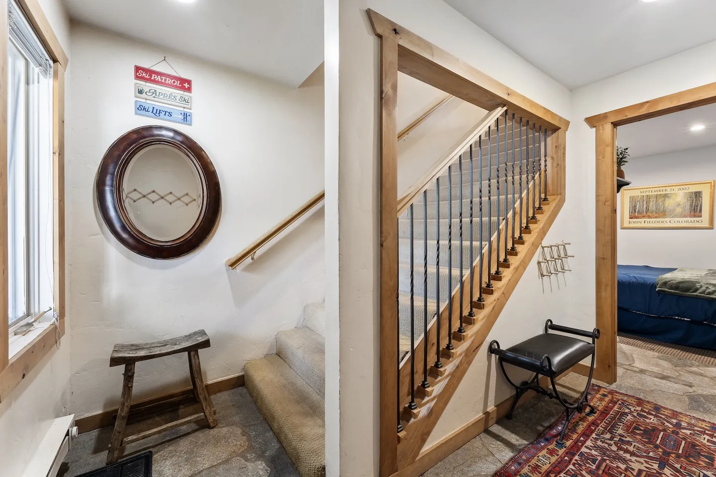Entryway with stone-look floors, a wooden bench, a round wall mirror, and a carpeted staircase framed with timber and metal railings.