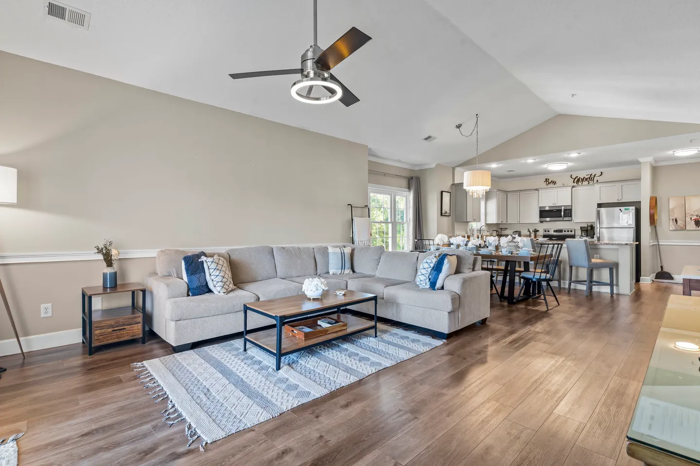 Open-concept living room with a large sectional sofa, coffee table, and area rug, extending toward a dining area and kitchen.