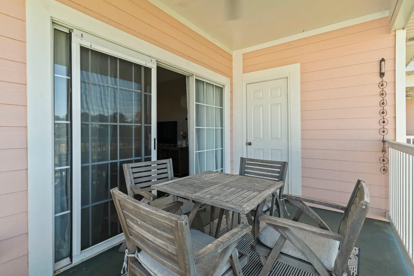 Covered balcony with pink horizontal siding, a square wooden patio table, and four matching wooden armchairs.