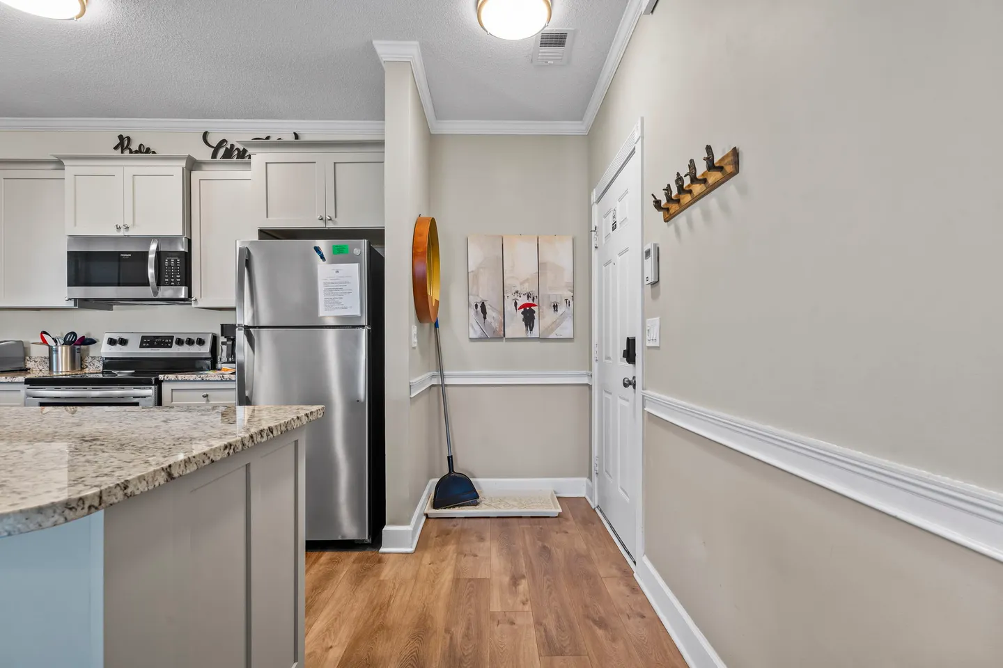 Hallway entrance leading into an open-concept kitchen with light wood-style flooring, white trim, and stainless steel appliances.