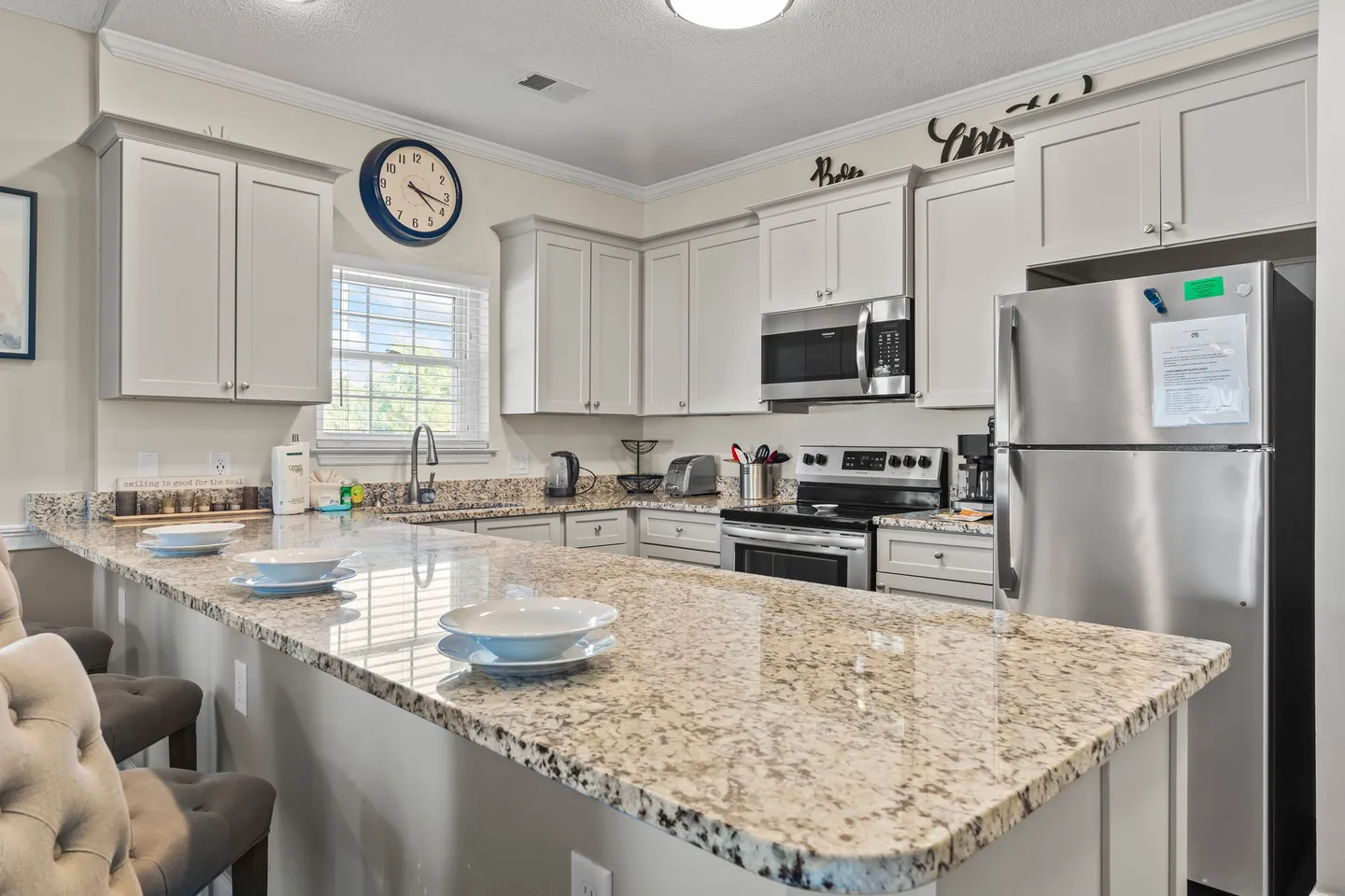 Kitchen with speckled granite countertops, white cabinetry, stainless steel appliances, and a breakfast bar set with dishes.