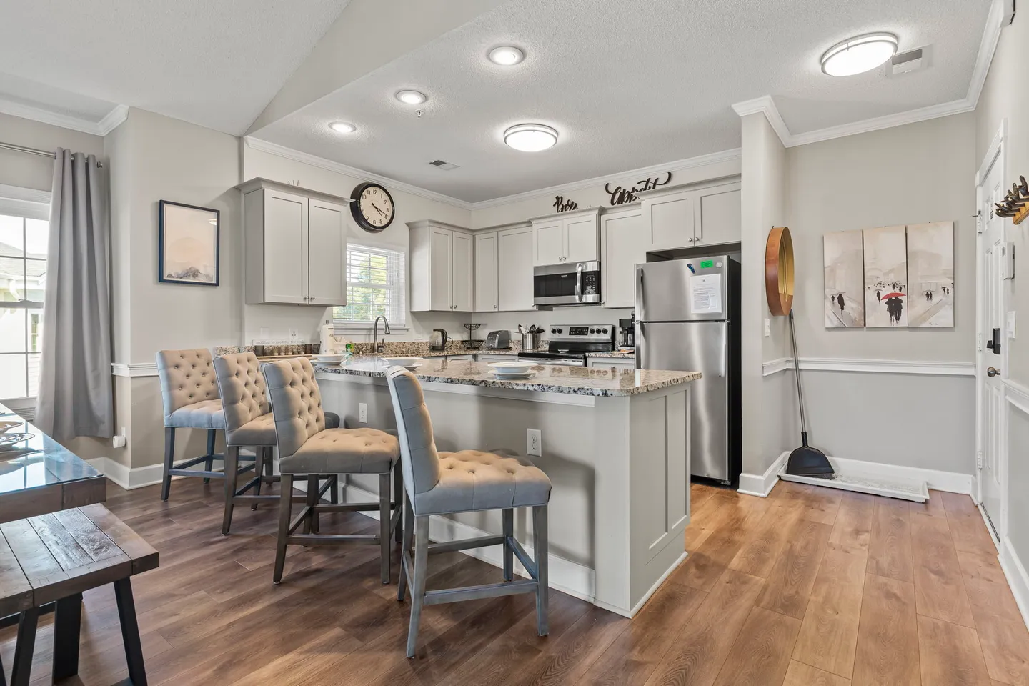 Kitchen with white cabinetry, granite breakfast bar with tufted stools, stainless steel appliances, and wood-look flooring.