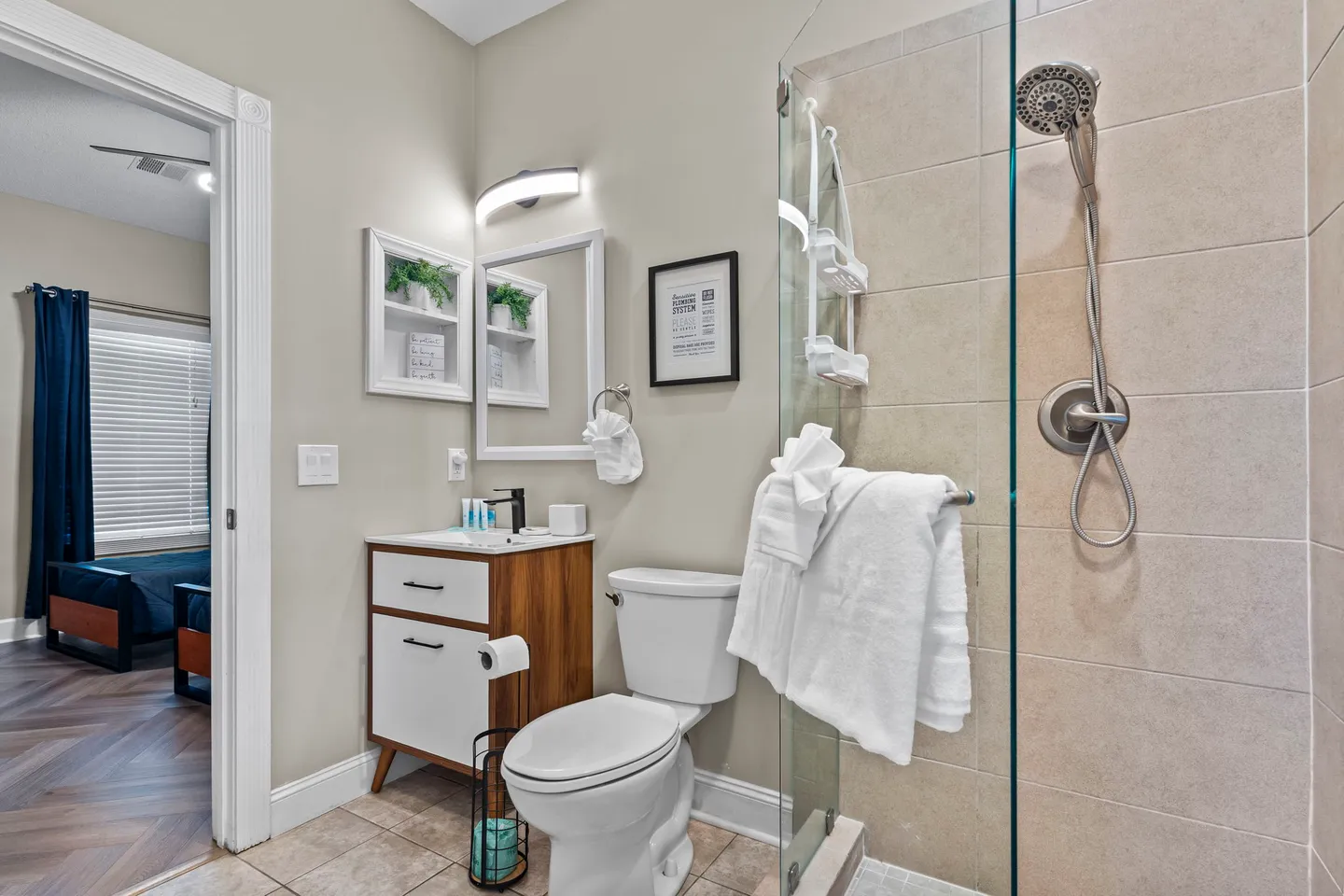 Bathroom featuring a glass-enclosed shower, toilet, and modern vanity with a view into an adjacent bedroom.