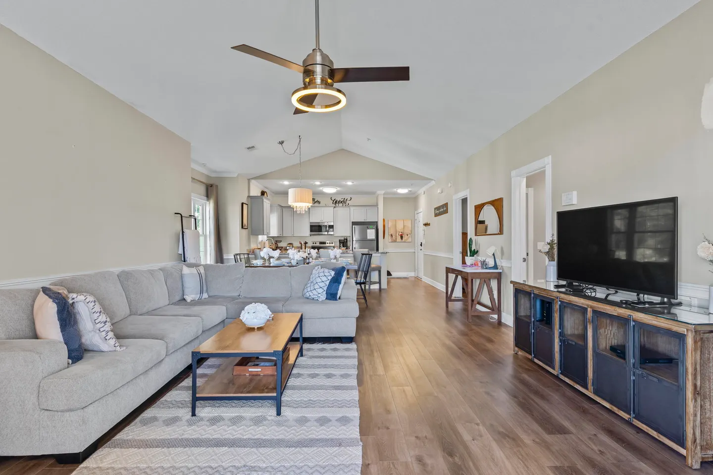 Open-concept living room with a large sectional sofa, coffee table, and TV credenza looking toward the kitchen and dining area.