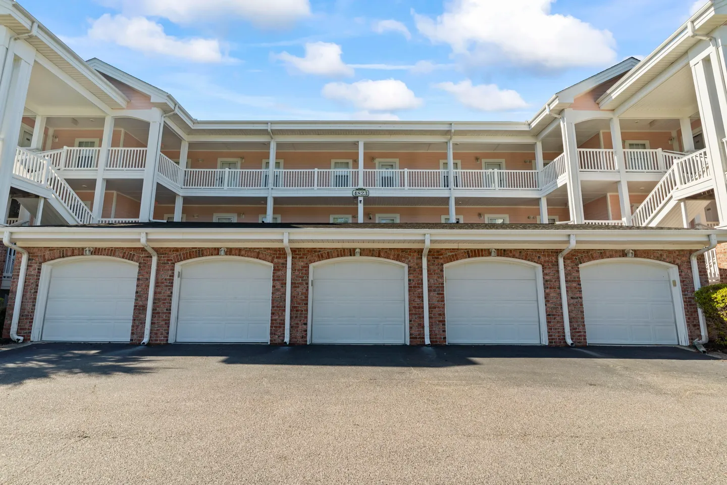 Exterior of a multi-story residential building with ground-floor garage bays and balconies above under a partly cloudy sky.