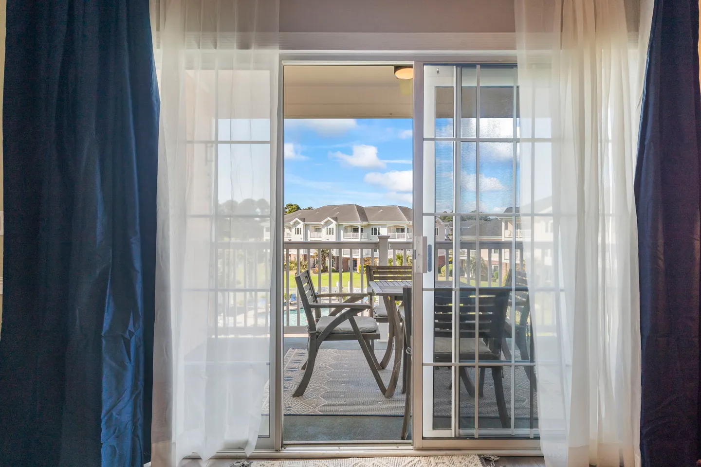 Sliding glass doors framed by curtains look out onto a covered balcony with patio furniture.