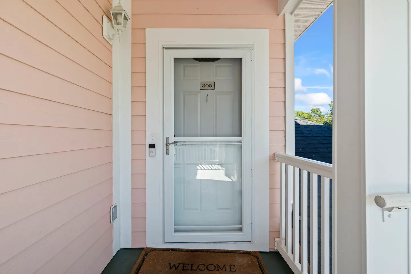 Front entry door with screen door and unit number 305 on a covered porch with peach siding.