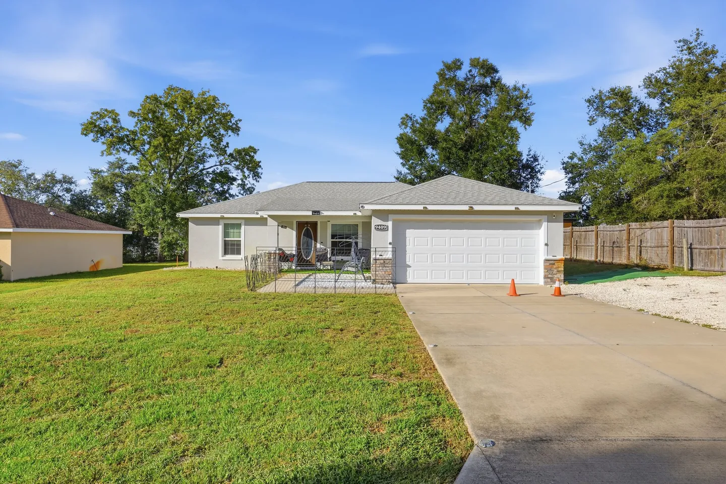 Exterior front view of a single-story home with a wide concrete driveway, green front lawn, and attached garage.