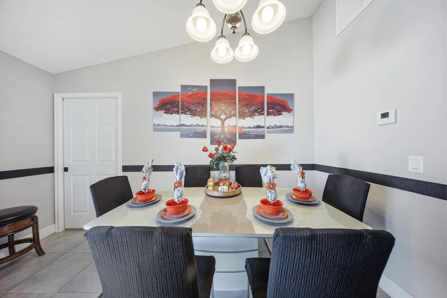 Dining area with a square table set for six, black high-back chairs, and multi-panel wall art.