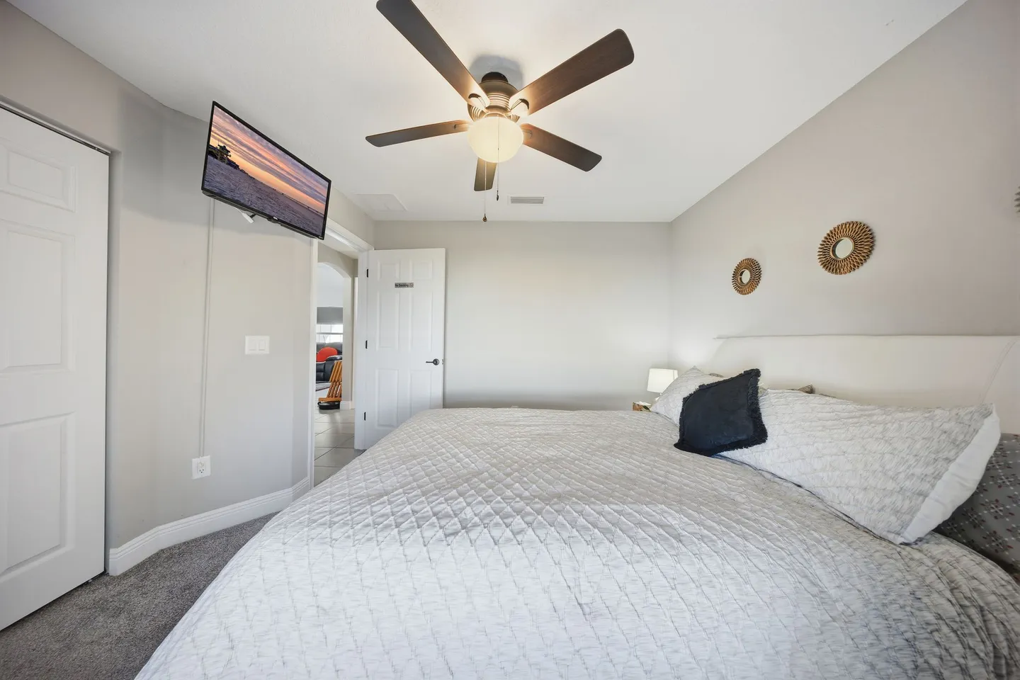 Bedroom featuring a made bed with white and gray bedding, a ceiling fan with light, and a wall-mounted TV.