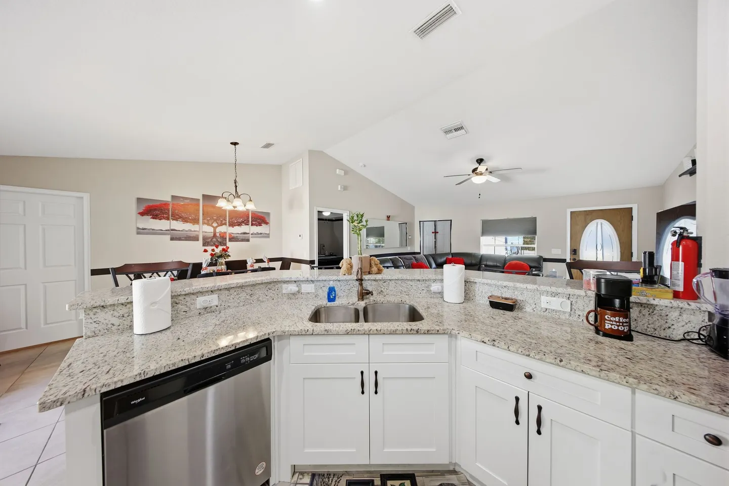 Kitchen counter with sink and dishwasher looking out towards the dining area and living room in an open-concept home.