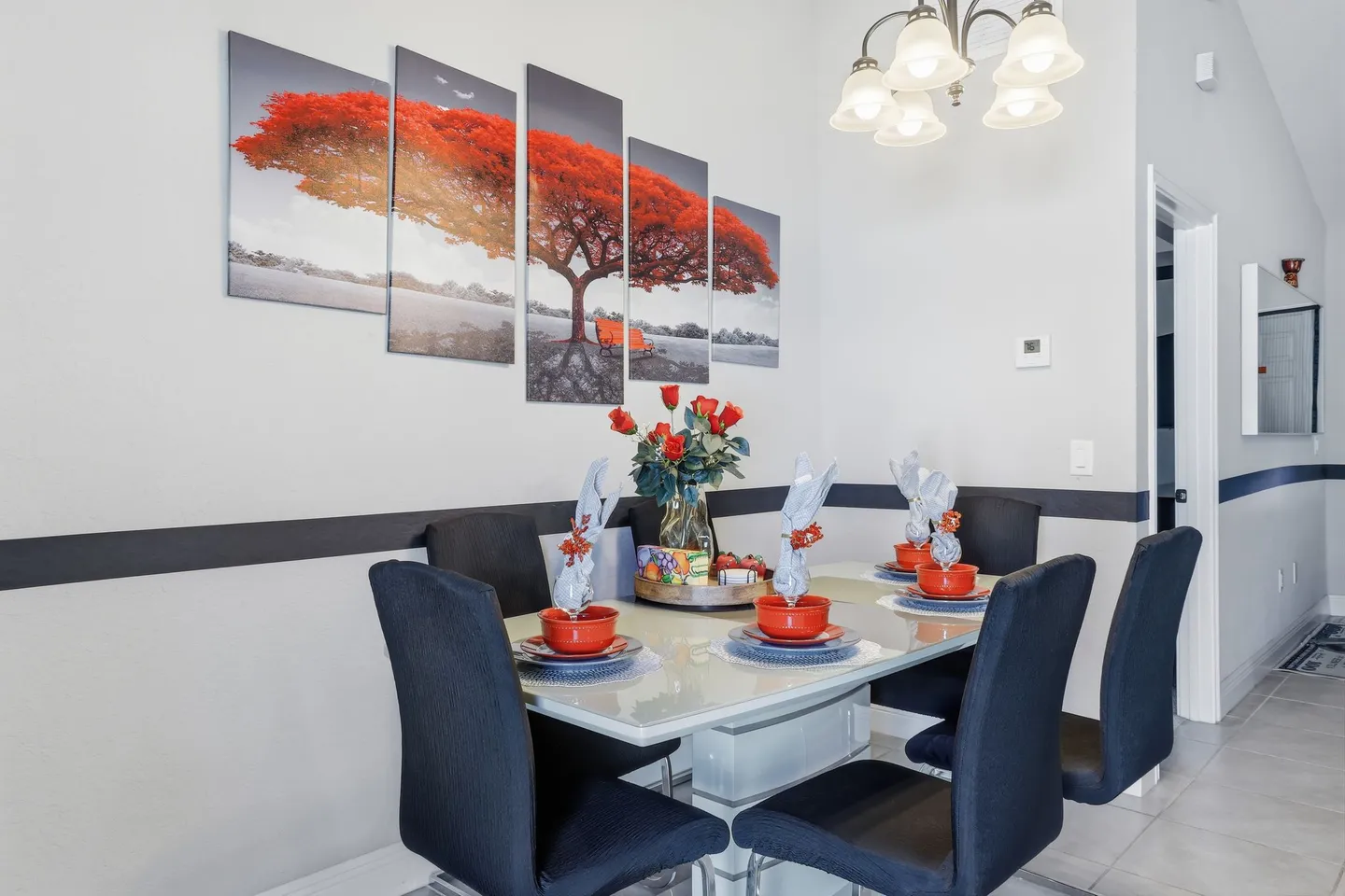 Dining area with a set table, dark upholstered chairs, a multi-panel canvas on the wall, and an overhead light fixture.