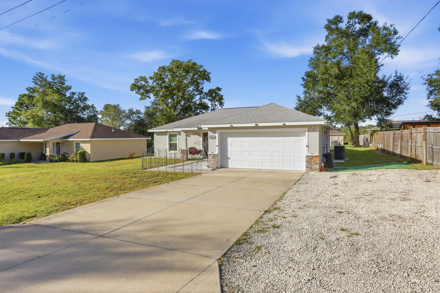 Exterior view of a single-story house with a two-car garage, concrete driveway, and front lawn under a clear sky.