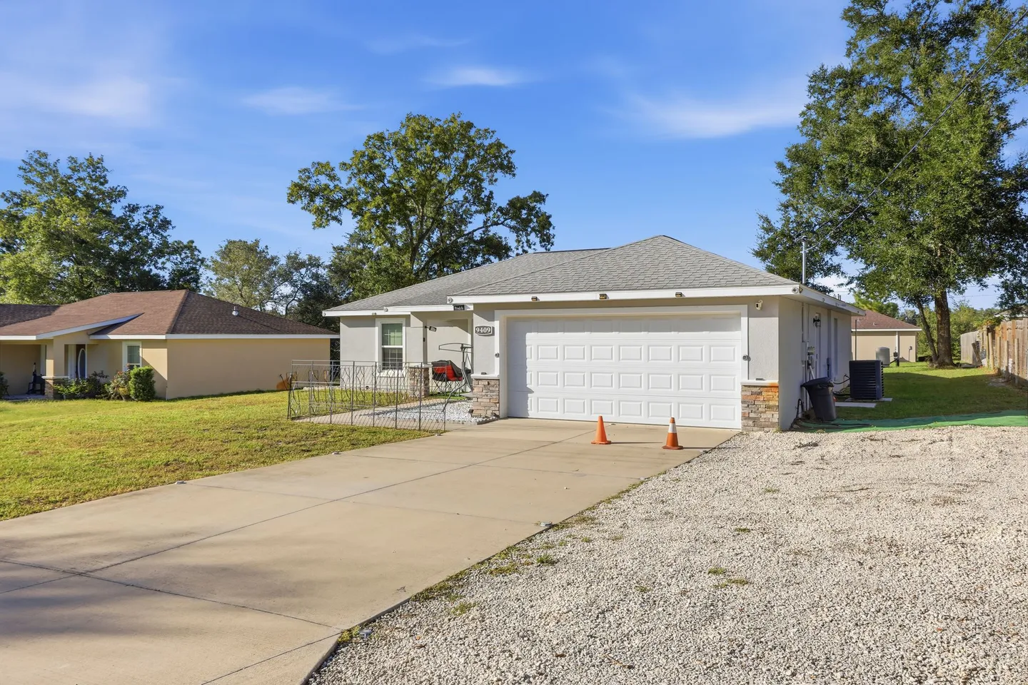 Front exterior of a single-story home with a white two-car garage, wide driveway, and grassy yard under a clear blue sky.
