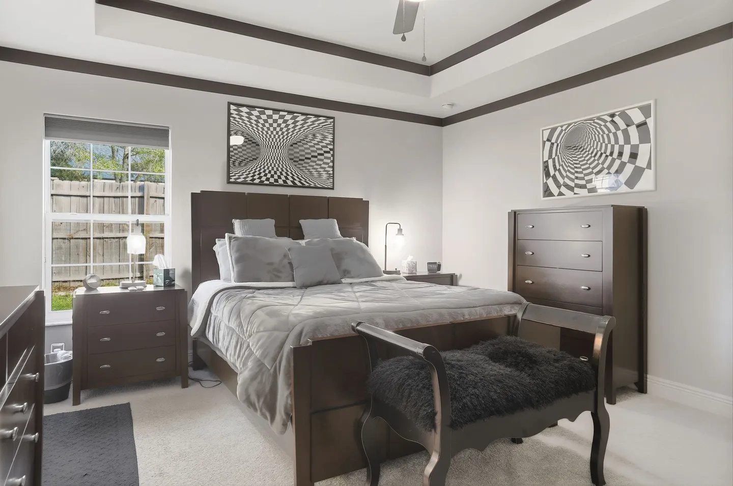 Bedroom with dark wood furniture, a tray ceiling, optical illusion wall art, and a bench at the foot of the bed.