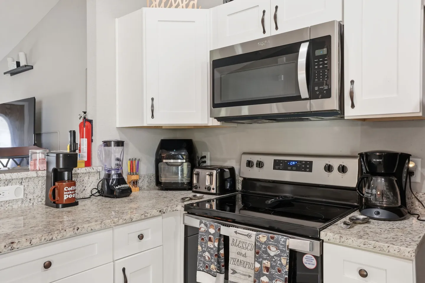 Kitchen counter with white cabinetry, stainless steel microwave, electric range, and small appliances like a coffee maker, blender, toaster, and air fryer.