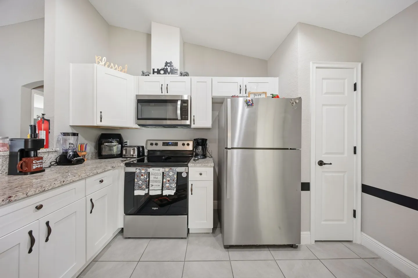 Kitchen with white cabinetry, stainless steel appliances including a refrigerator and electric range, and light tile flooring.
