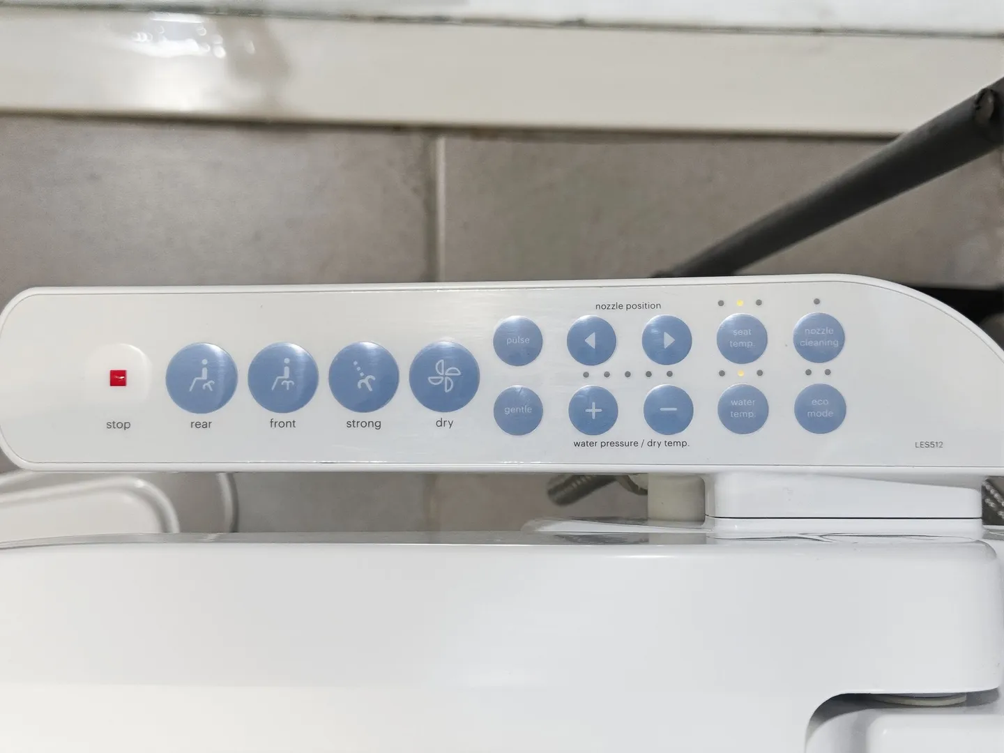 Close-up of an electronic bidet toilet seat control panel with labeled blue buttons.