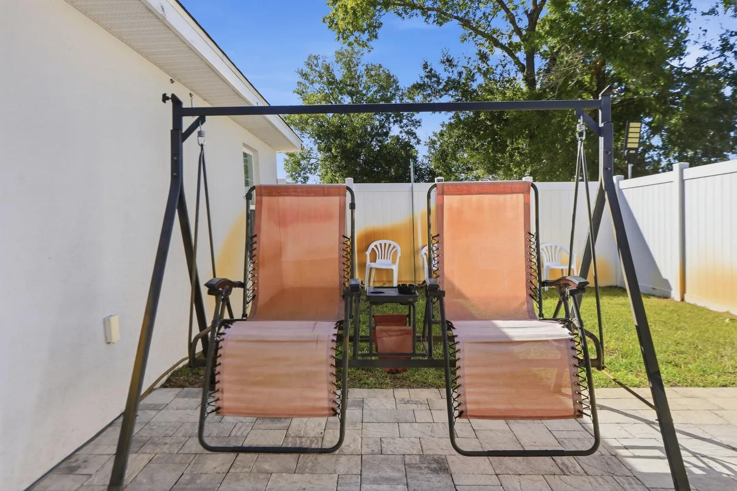 A dual outdoor swing bench with pinkish fabric seats on a stone paver patio in a fenced backyard.