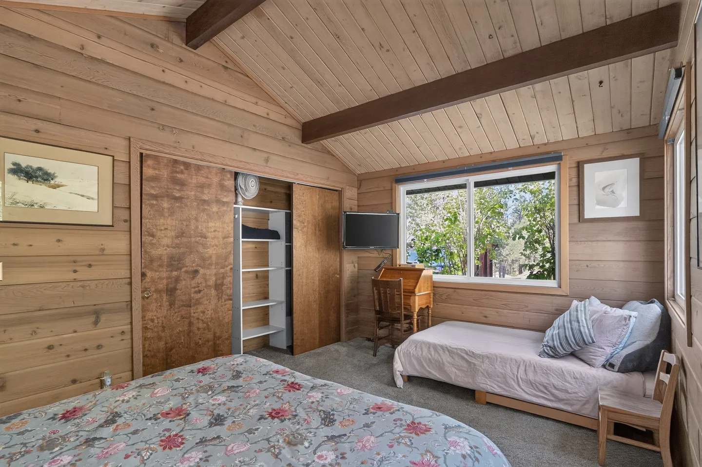 Bedroom with wood-paneled walls and ceiling, a floral bed, a daybed beneath a window, and a built-in closet.
