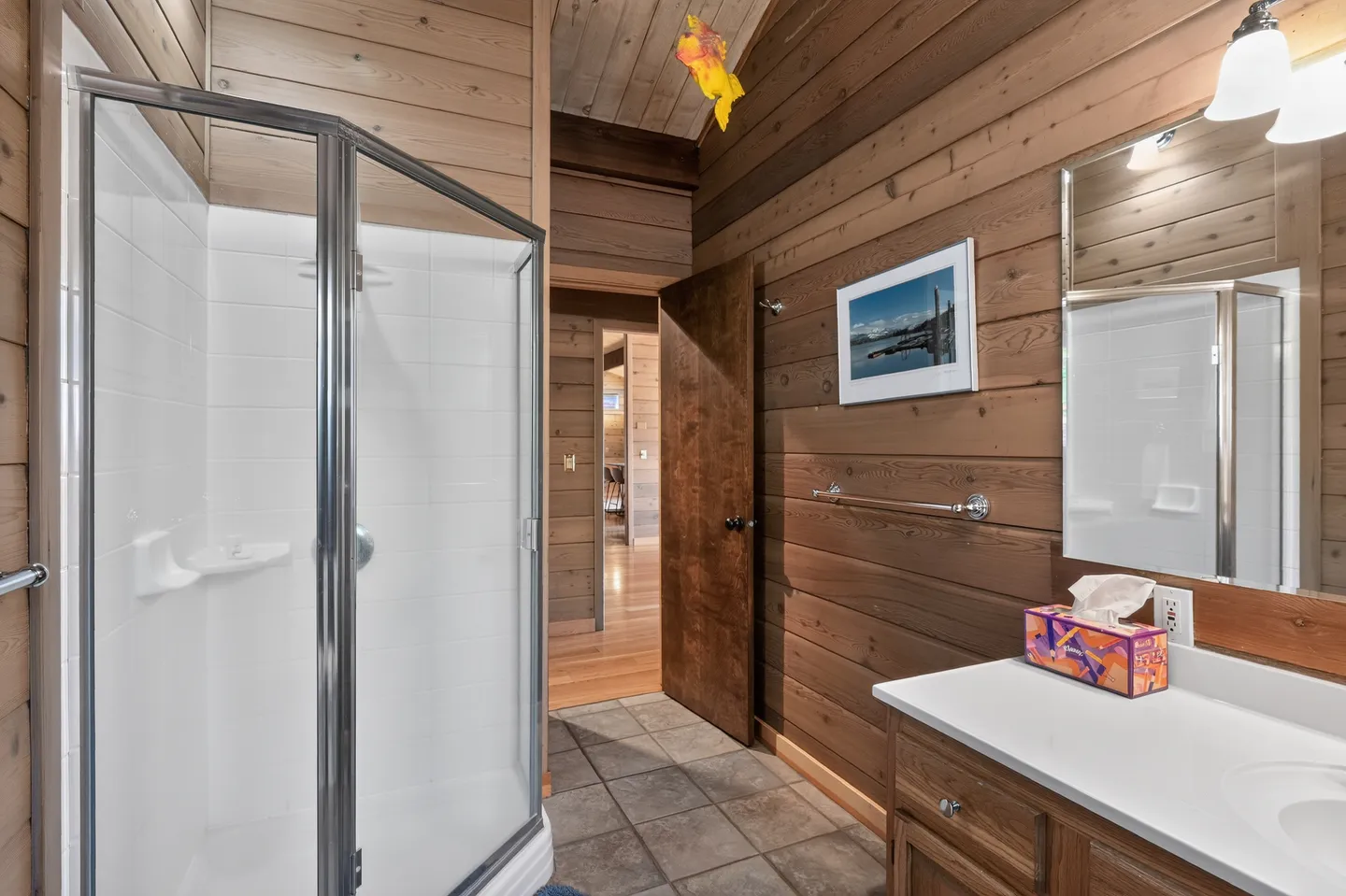 Bathroom with wood-paneled walls, tile flooring, a glass-door corner shower, and a vanity with a mirror.