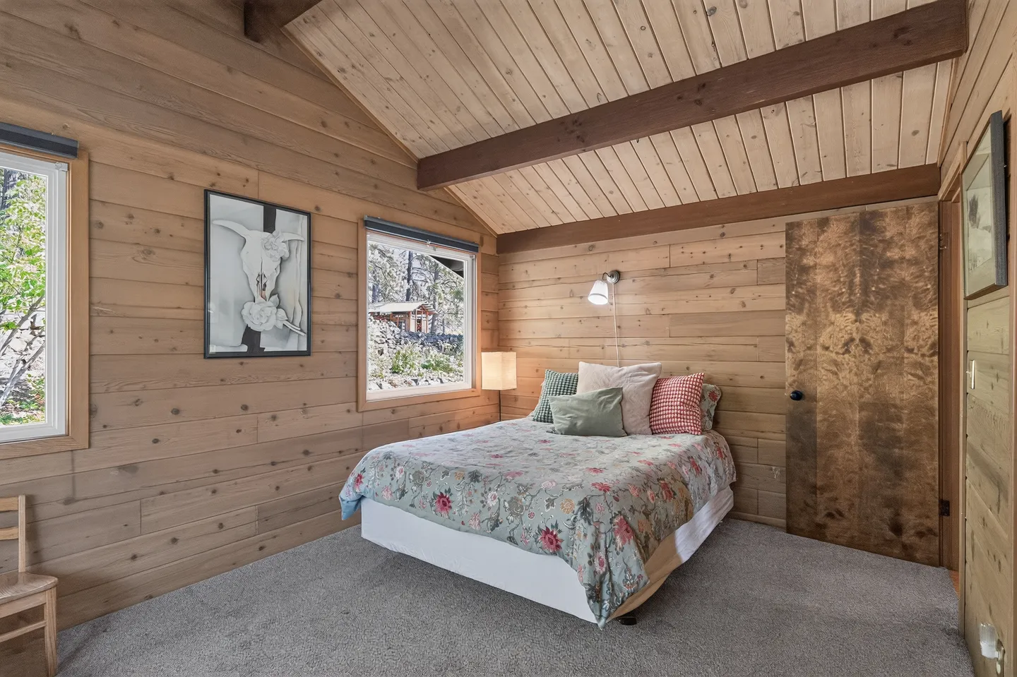 Bedroom with wood-paneled walls, vaulted ceiling with exposed beams, carpet, and a bed with a floral comforter.