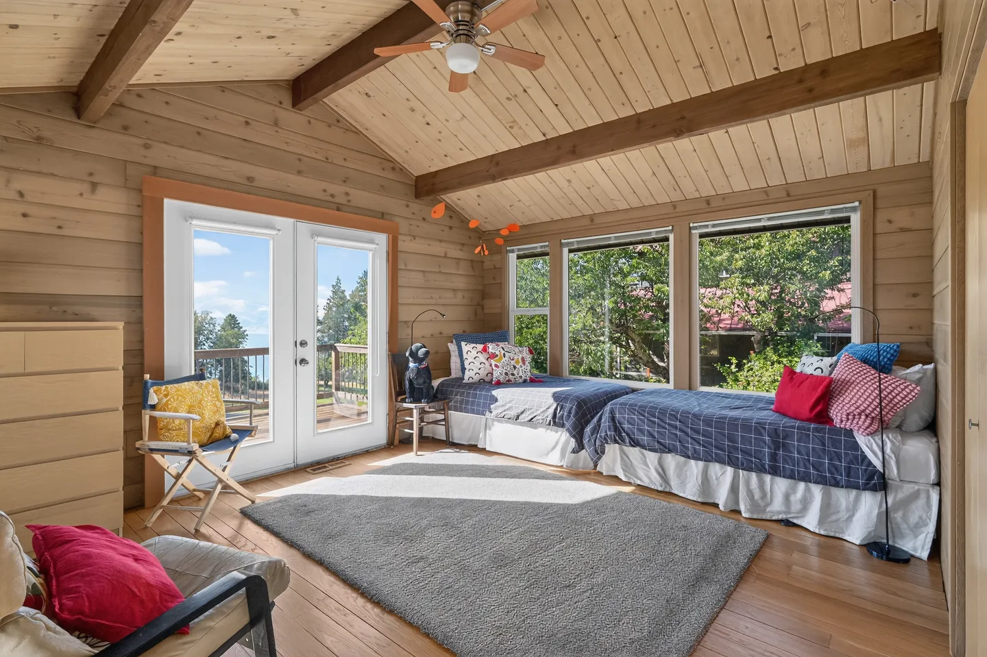 Bedroom with wood-paneled walls and ceiling, two twin beds, double glass doors leading to a deck, and large windows.