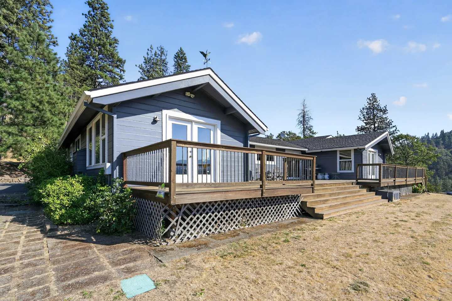 Exterior of a blue house with an elevated wooden deck and lattice skirting under a clear blue sky.
