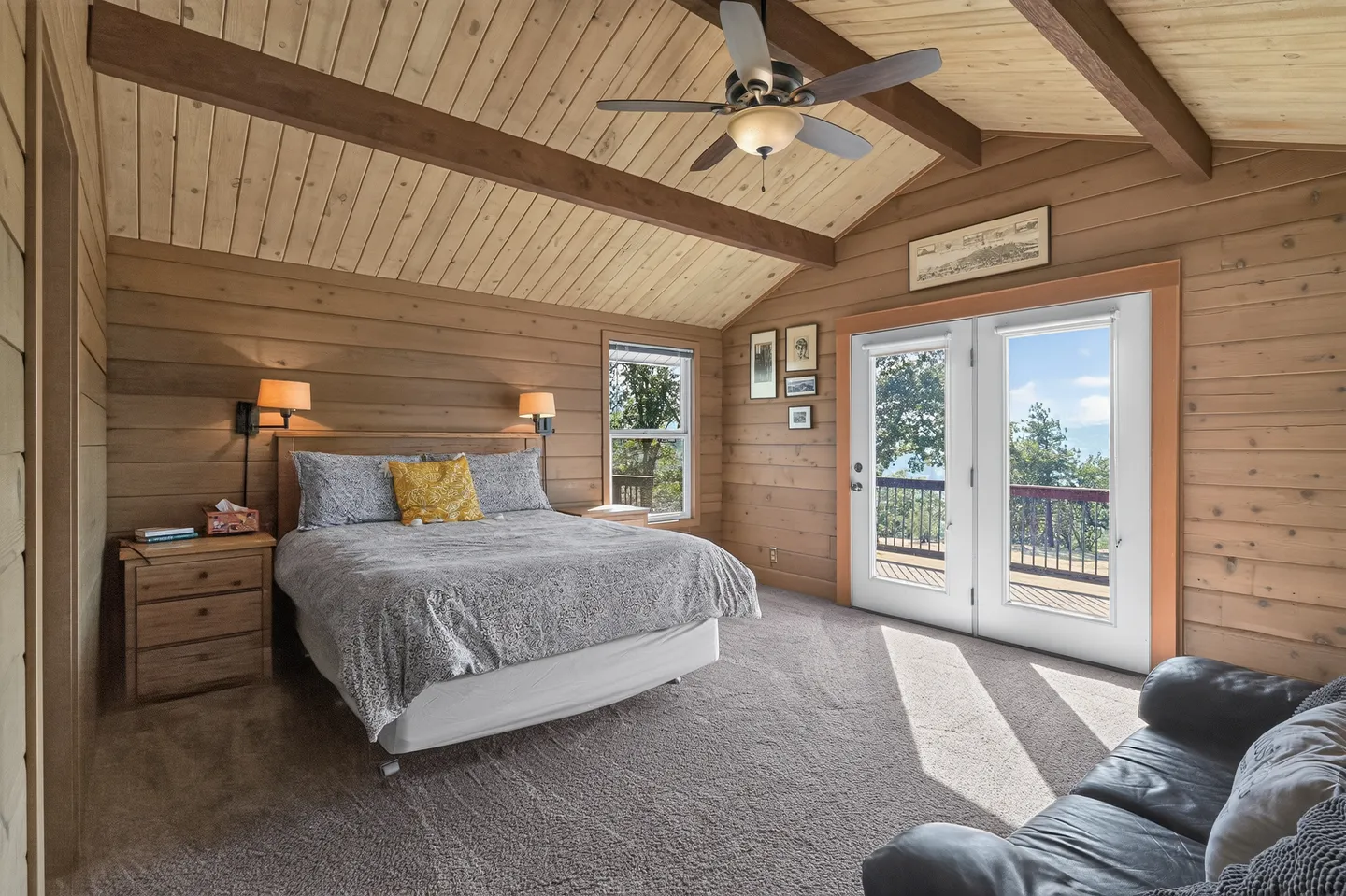 Bedroom with wood-paneled walls and ceiling, carpeted floor, double bed, and glass doors opening to a balcony.