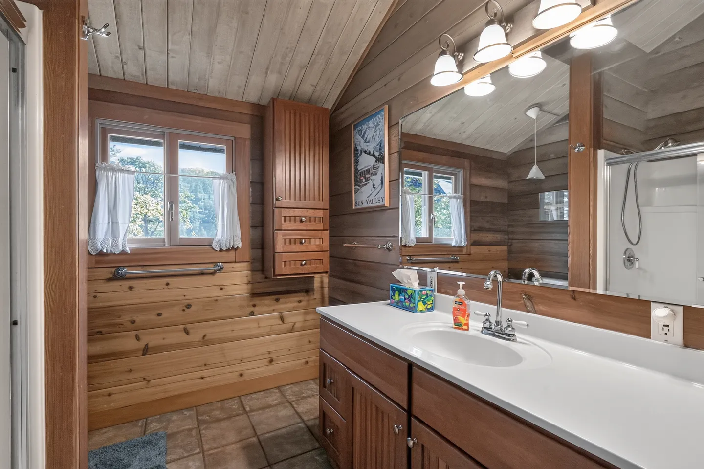 Bathroom with wood-paneled walls and ceiling, a white vanity countertop with sink, large mirror, and a window.