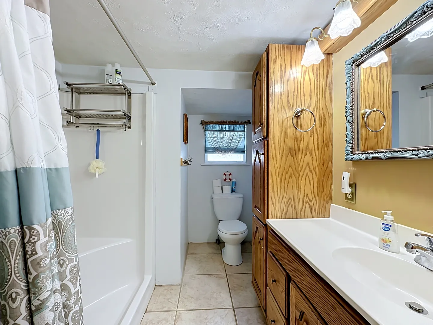 Bathroom with a wood vanity, tiled floor, step-in shower stall, and a toilet tucked into a rear alcove beneath a window.
