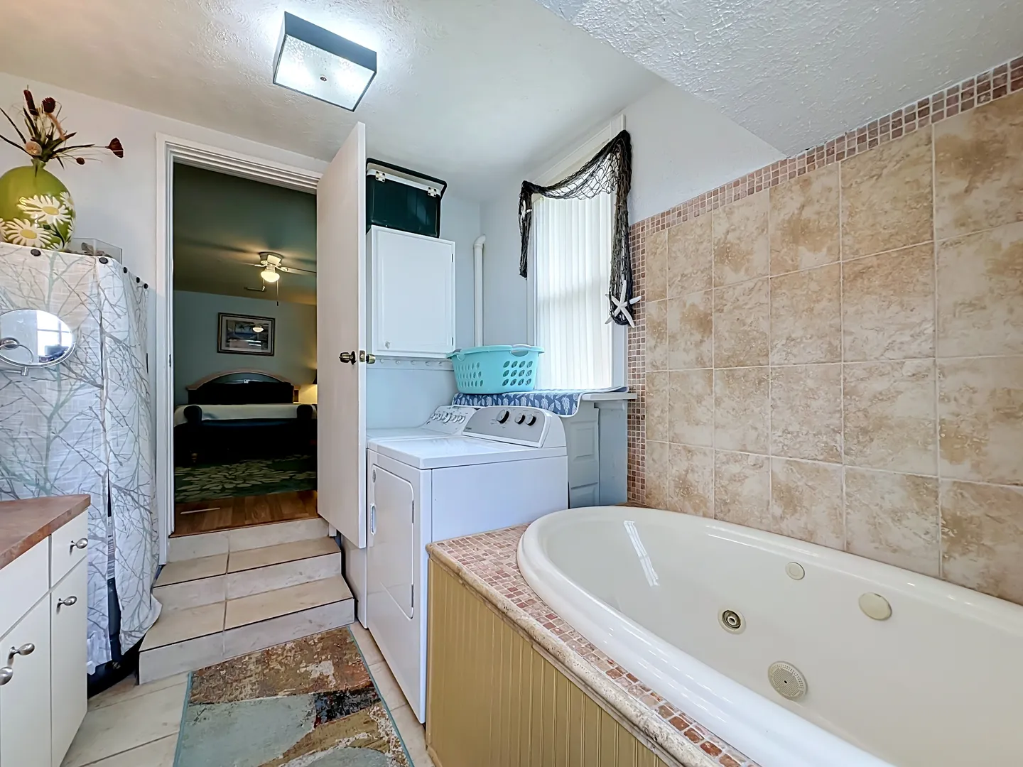 Bathroom with a tiled soaking tub, washer and dryer, and steps leading to an adjacent bedroom.