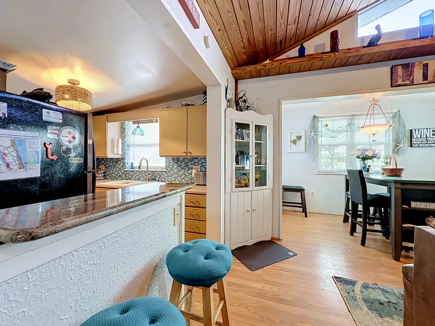 Open-concept living space showing kitchen counter with barstools, wood-paneled angled ceiling, and dining area.