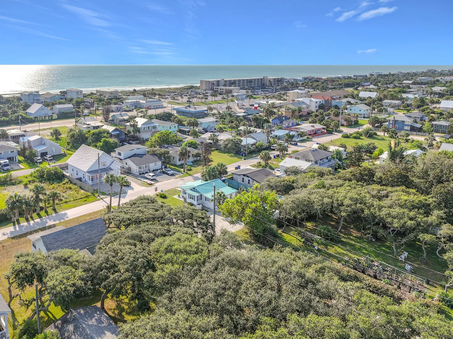 Aerial view of a coastal neighborhood with houses, lush green trees, and the ocean along the horizon.