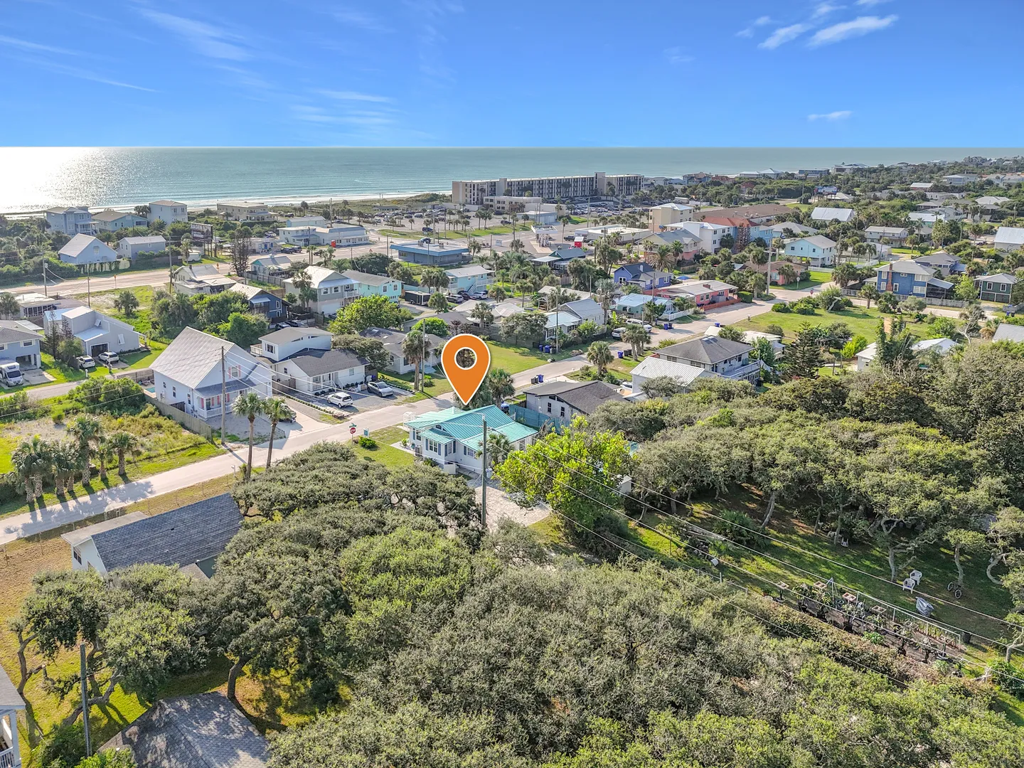 Aerial view of a coastal neighborhood with a location marker above a single-story house near the ocean.